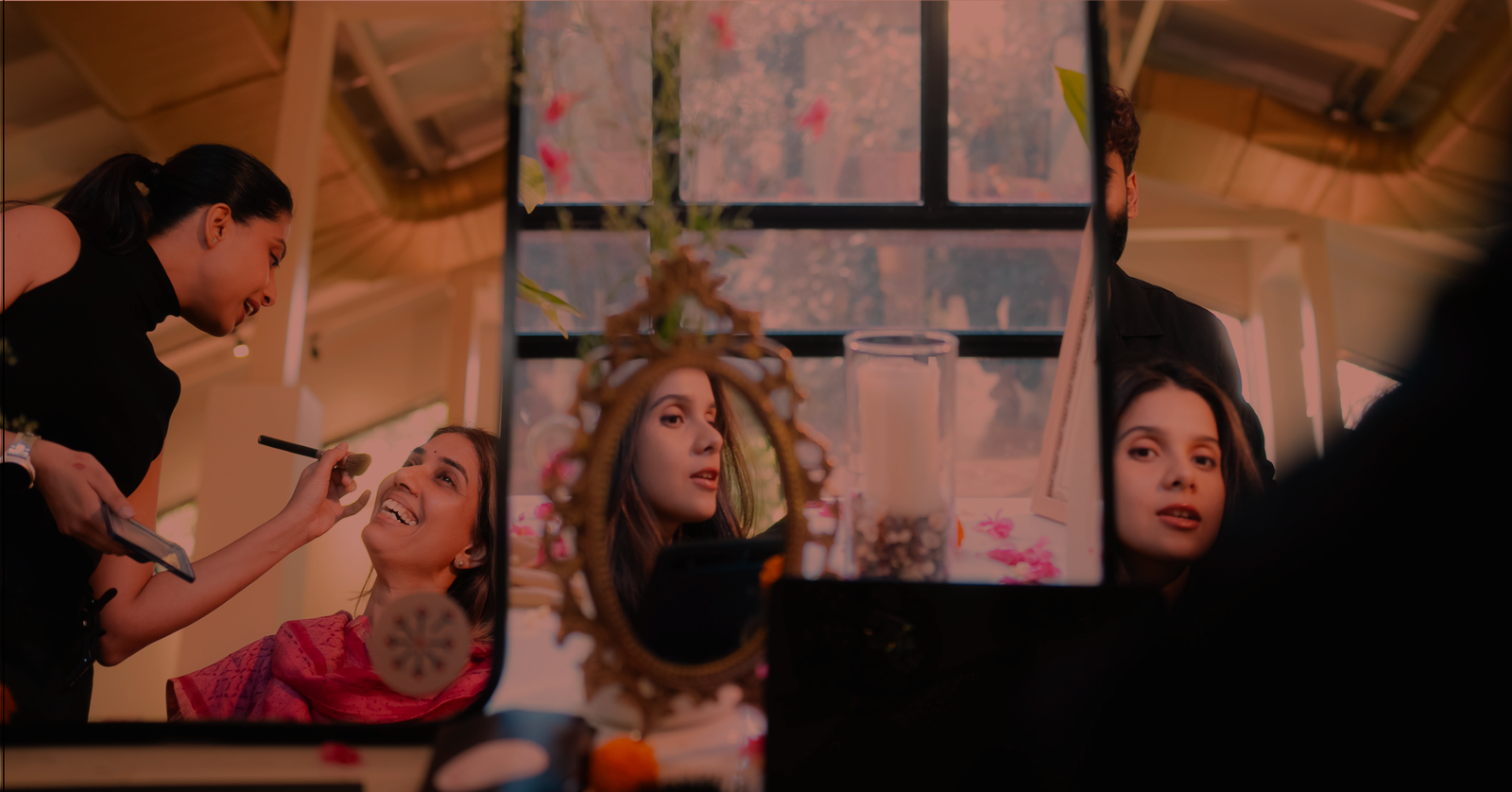 An artist applying makeup to a smiling guest, reflected in mirrors at a getting-ready sanctuary
