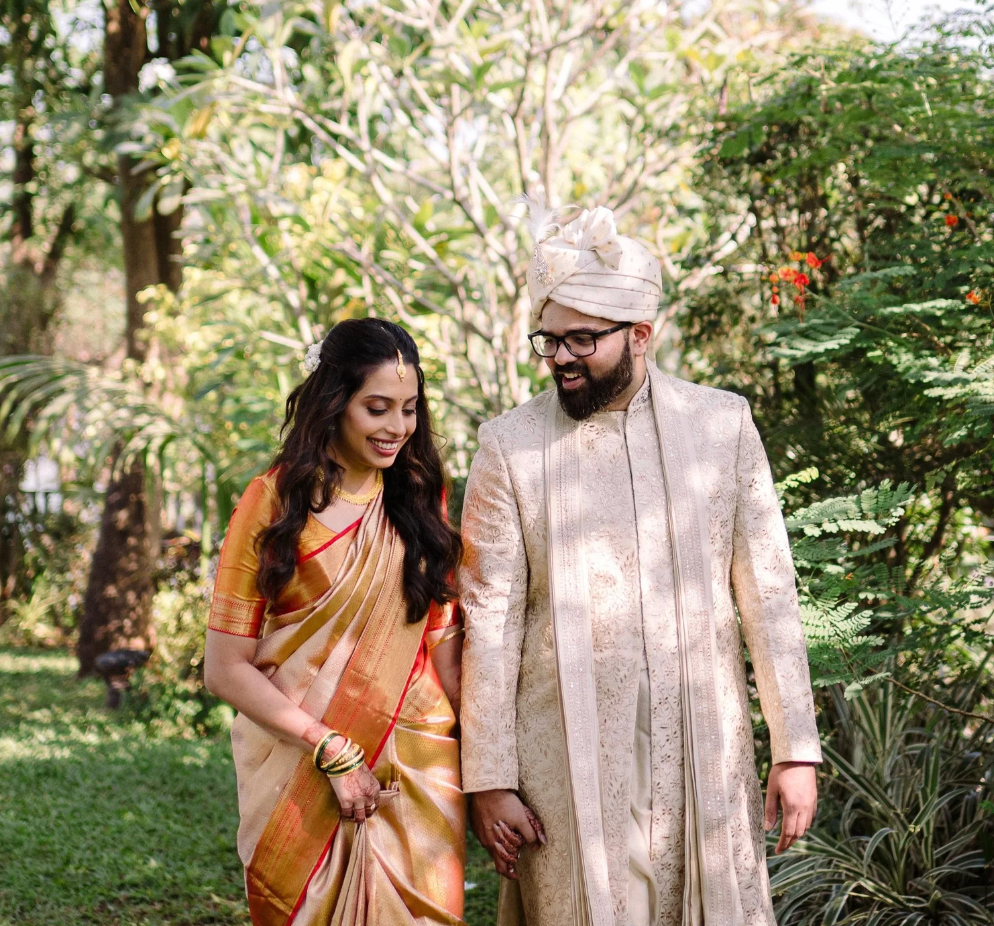A bride surrounded by her guests, all dressed in gold and maroon sarees